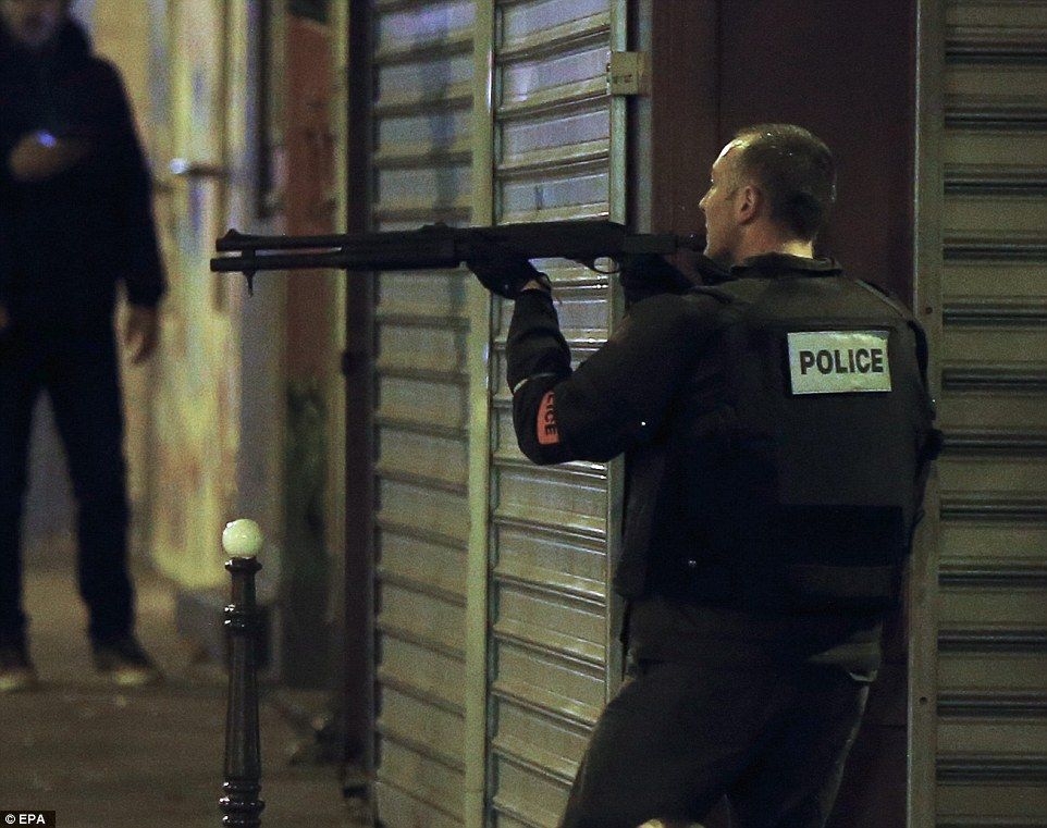 A French police officer takes cover while on the lookout for the shooters who attacked the restaurant ‘Le Petit Cambodge’