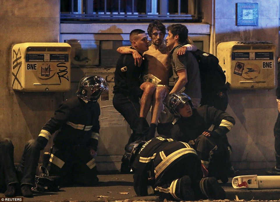 French fire brigade members help an injured individual near the Bataclan concert hall following fatal shootings in Paris, France.